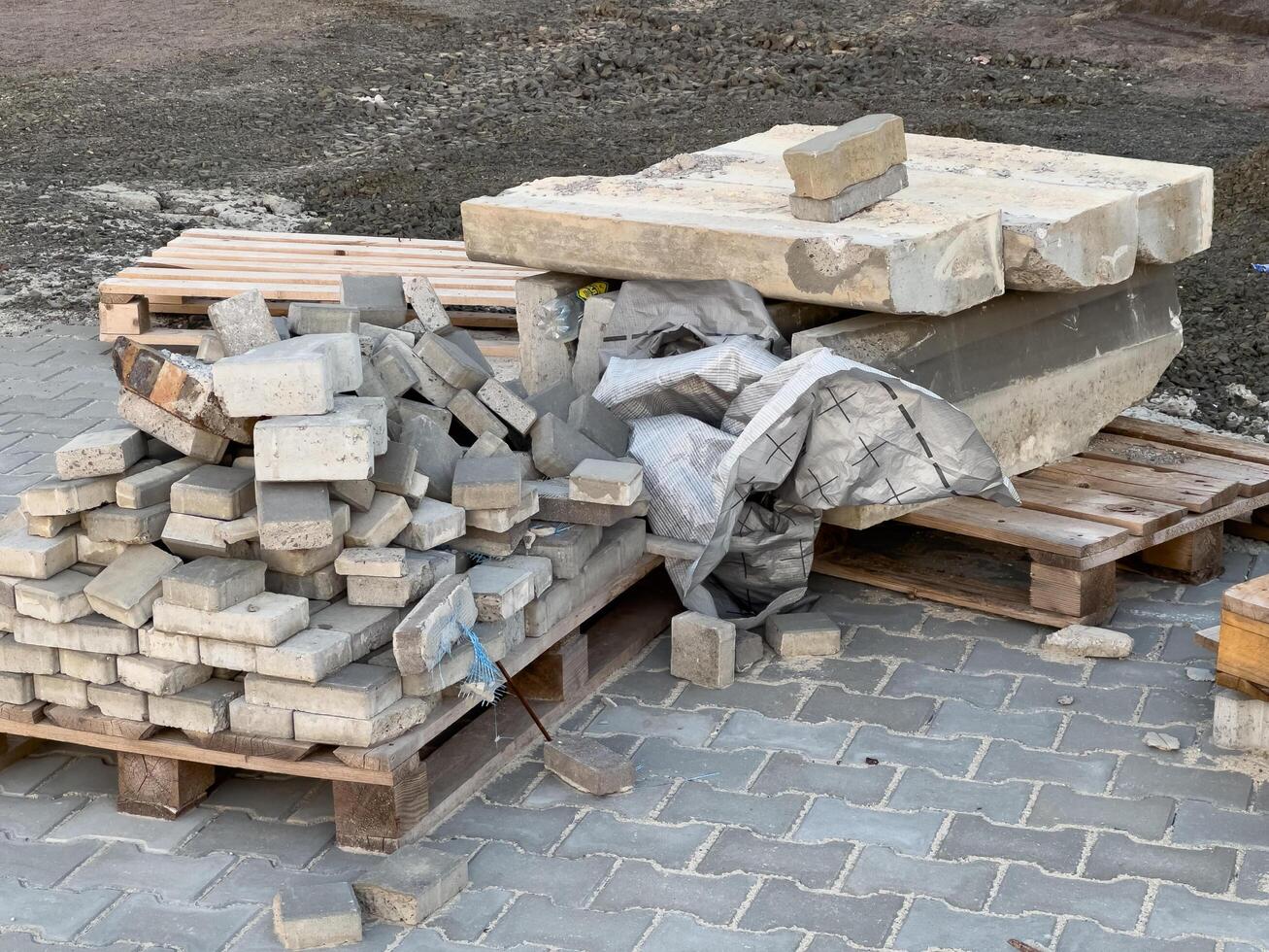 Concrete blocks and slabs are organized on pallets at a construction site, surrounded by gravel and construction debris in bright daylight photo