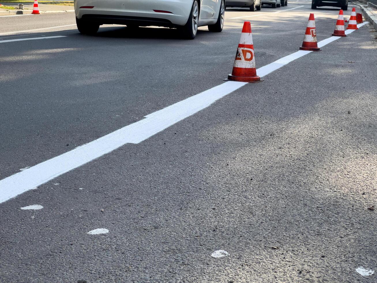 Traffic cones mark freshly painted white line on asphalt, indicating ongoing road work in an urban setting during the day photo