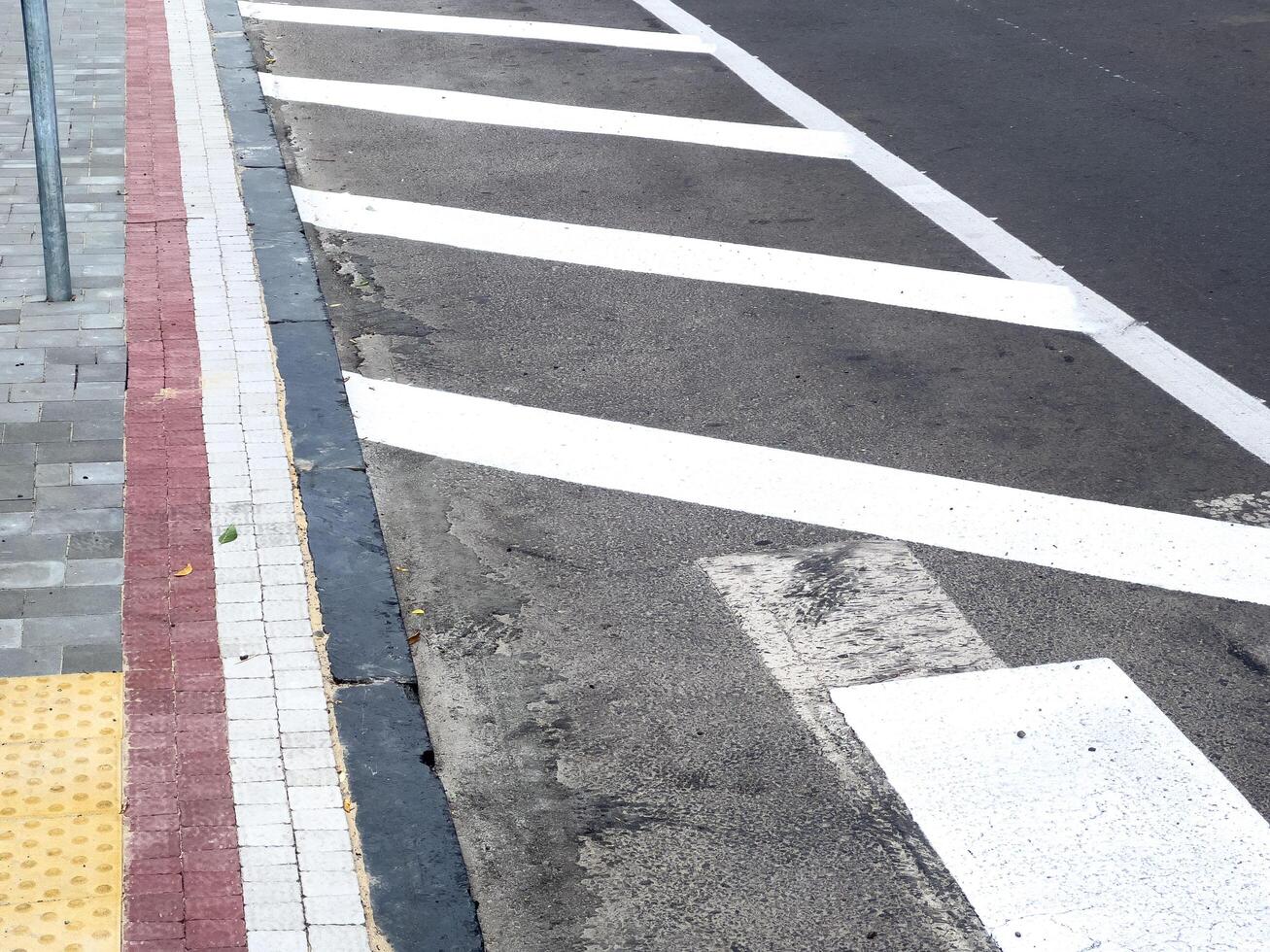 A clearly marked pedestrian crossing is visible alongside a textured sidewalk and road surface under bright sunlight in an urban area photo