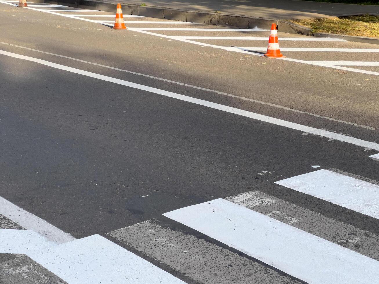 Traffic cones are positioned around a pedestrian crossing as roadwork takes place on a busy urban street during daylight hours photo