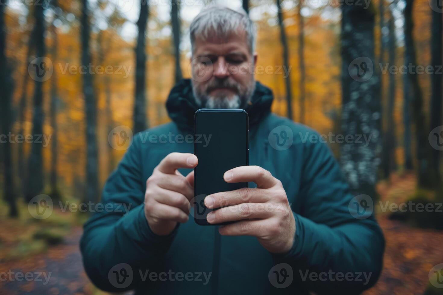 Bearded man capturing autumn colors with smartphone in forest photo