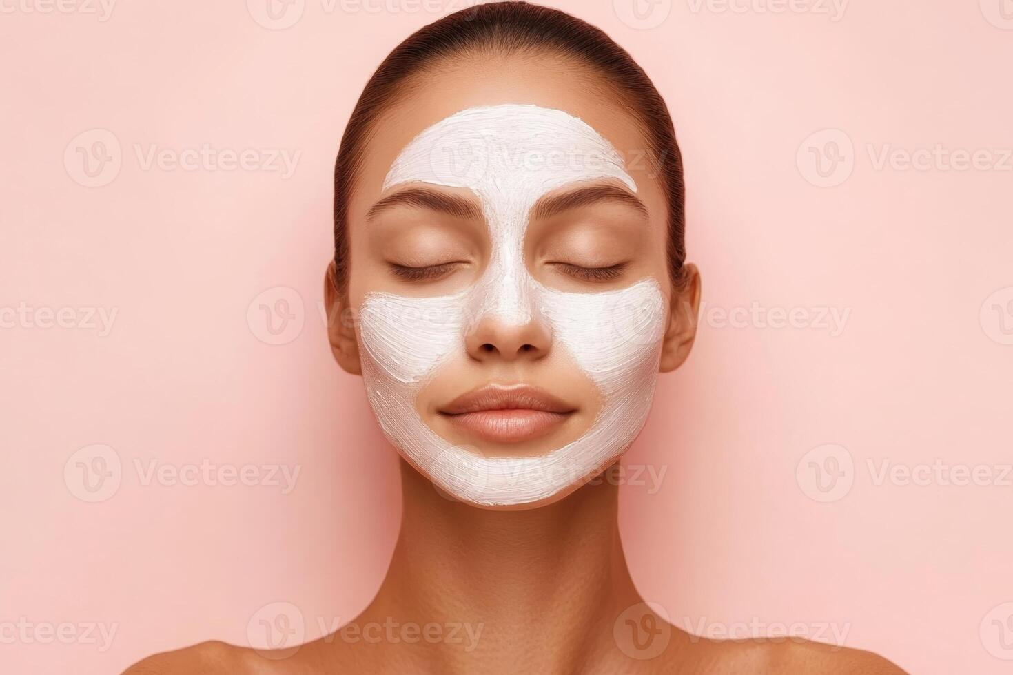 Skincare routine featuring a woman applying a facial mask on smooth skin against a pastel pink background photo