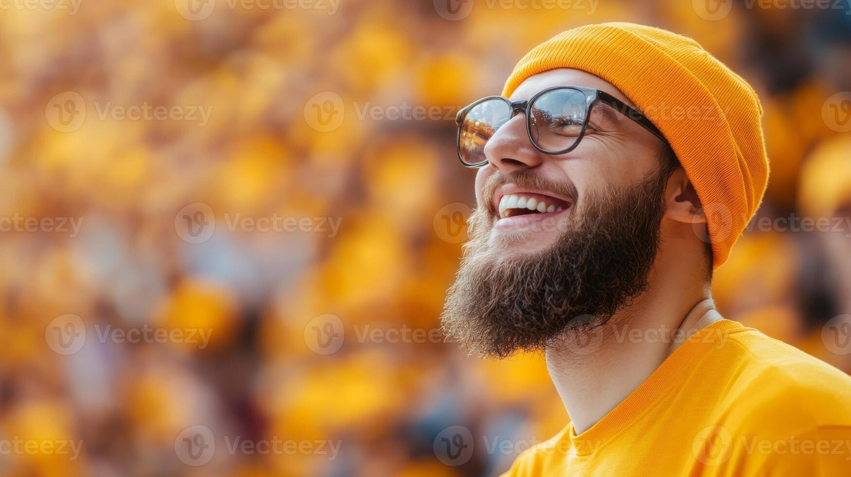 Joyful young man in orange attire smiling and enjoying a festive atmosphere at an outdoor event with a crowd in the background photo