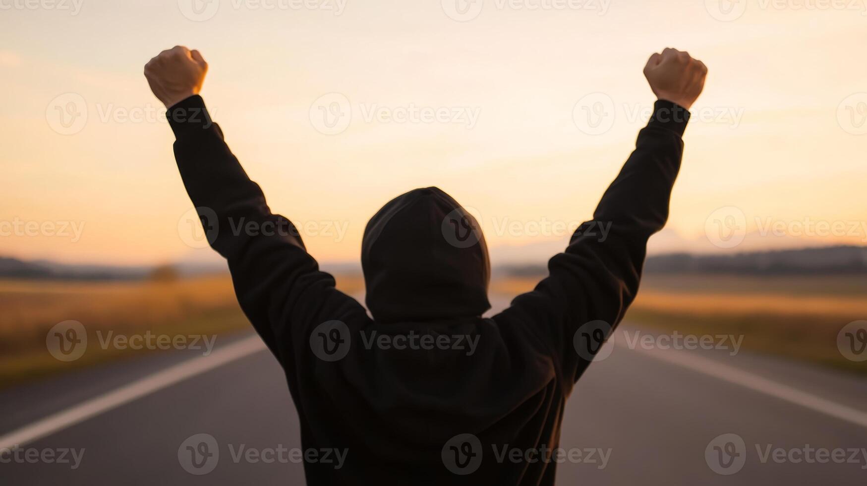 Victory moment of a young person celebrating success outdoors at sunset on an open road photo