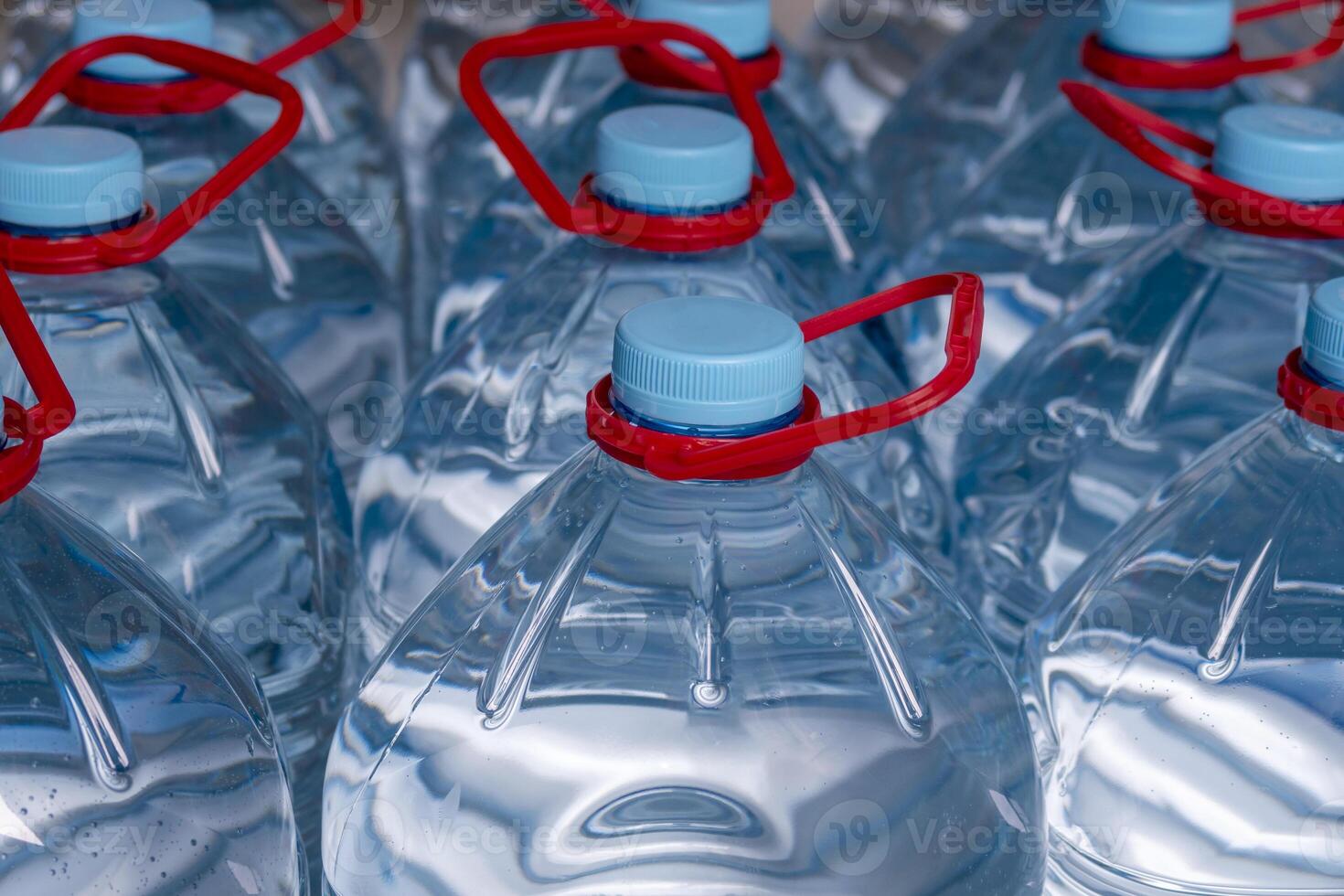 5 liter bottles with drinking water. Blue covers and red handles. Selective focus. photo