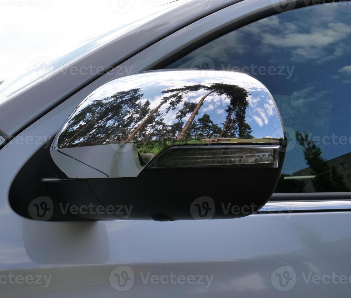 Trees reflected in chrome car mirror trim closeup stock photo