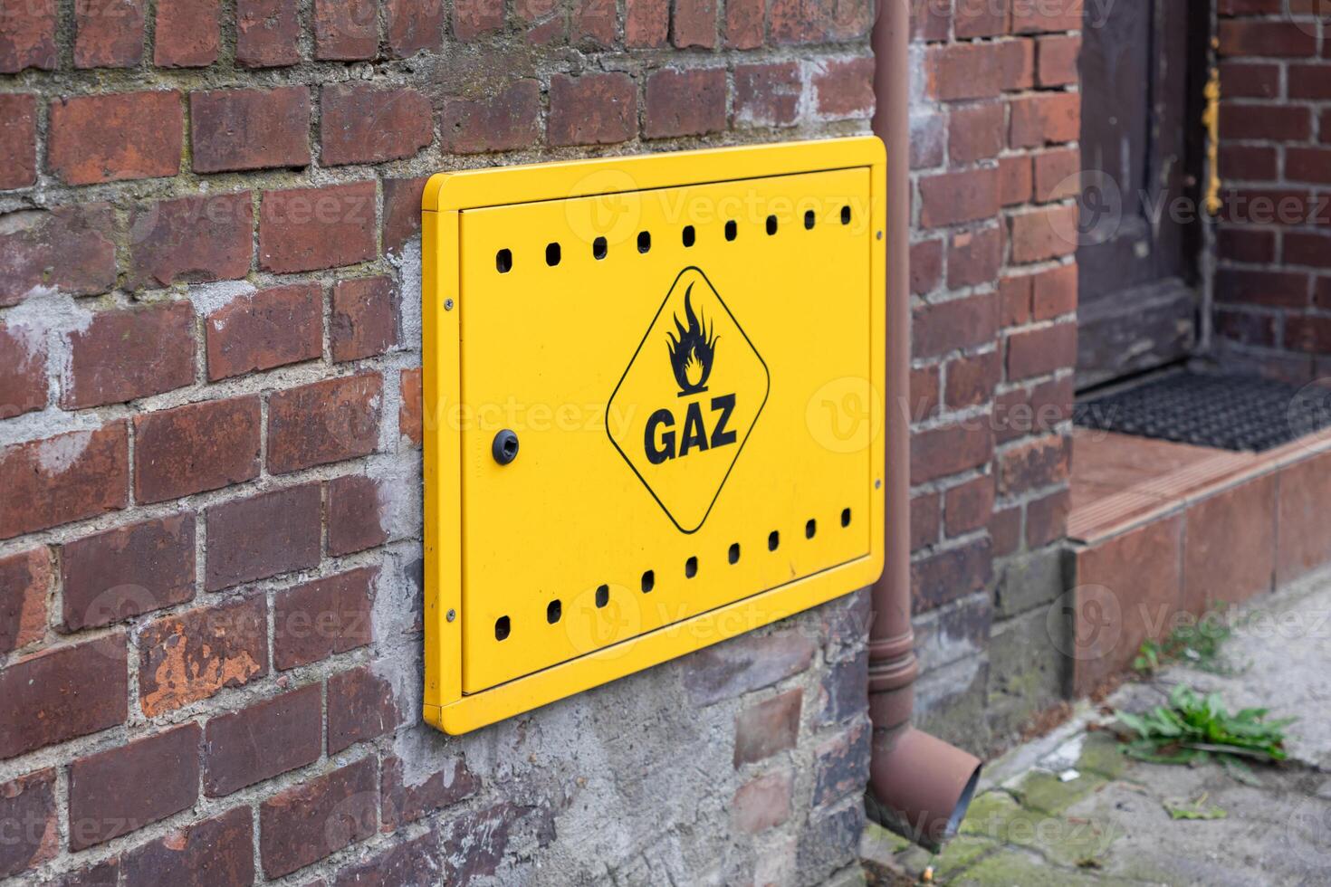 Bright yellow gas meter box displaying GAZ text and flame symbol mounted on an aged brick wall, symbolizing residential energy supply and essential utility infrastructure photo