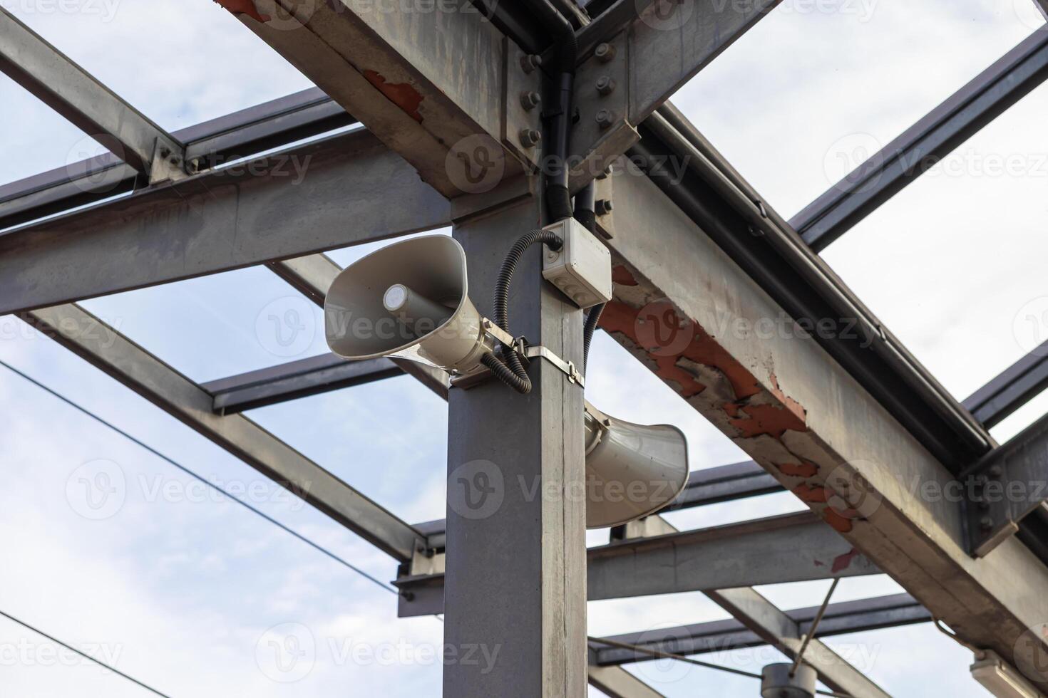 Grey horn loudspeakers mounted on a sturdy industrial metal beam structure, signifying a public address system for crucial announcements and safety photo