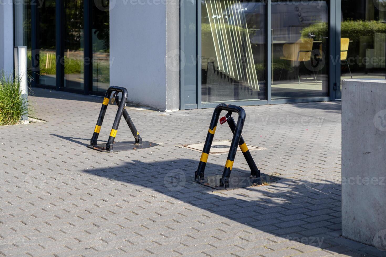 Two black and yellow foldable parking barriers with a red padlock secure reserved spots on a paved lot, ensuring private vehicle access control outside a modern office building photo