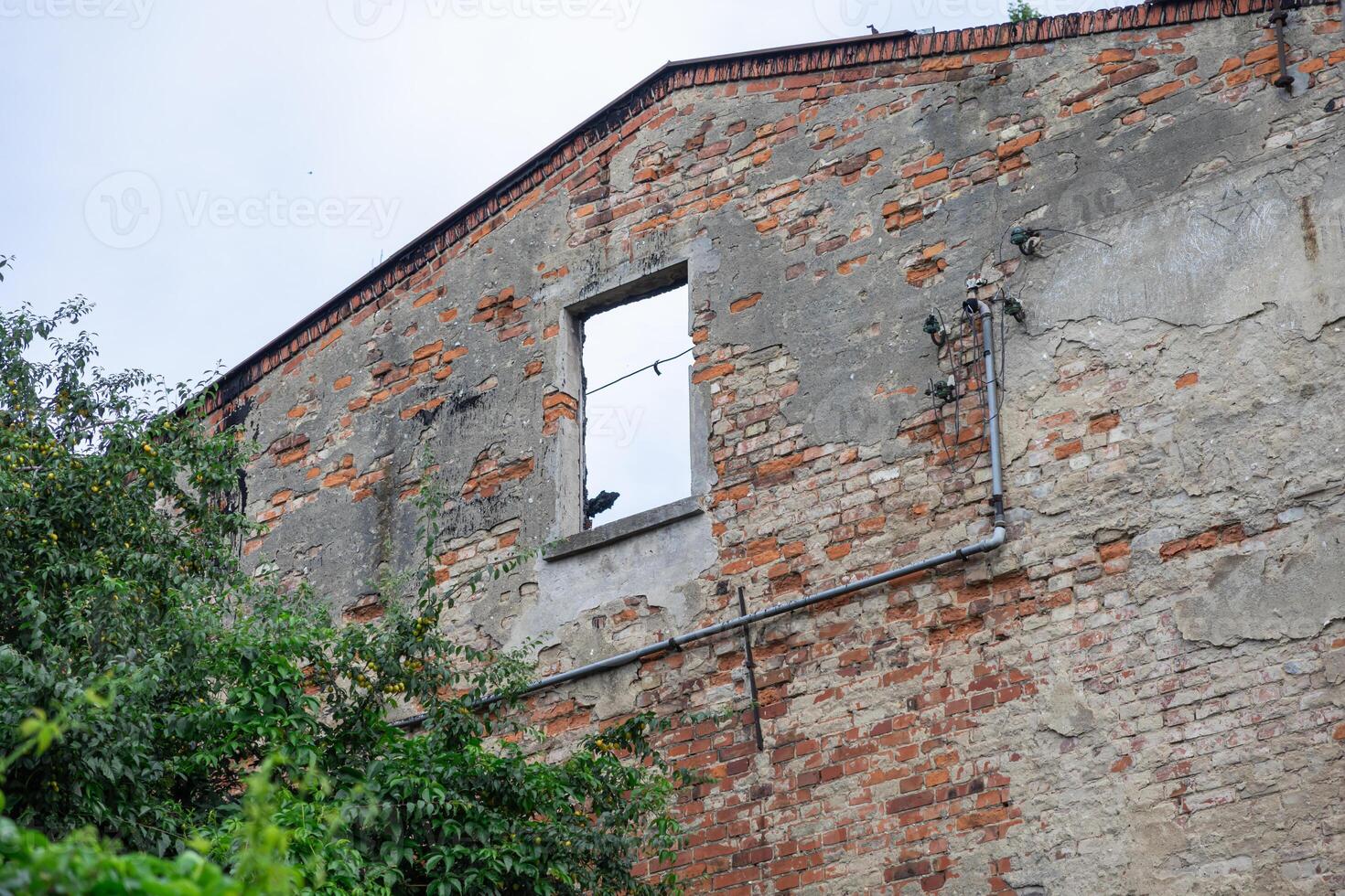 Dilapidated brick wall of an old abandoned building with a broken window, exposed plaster, and pipes, symbolizing urban decay and historical ruin photo