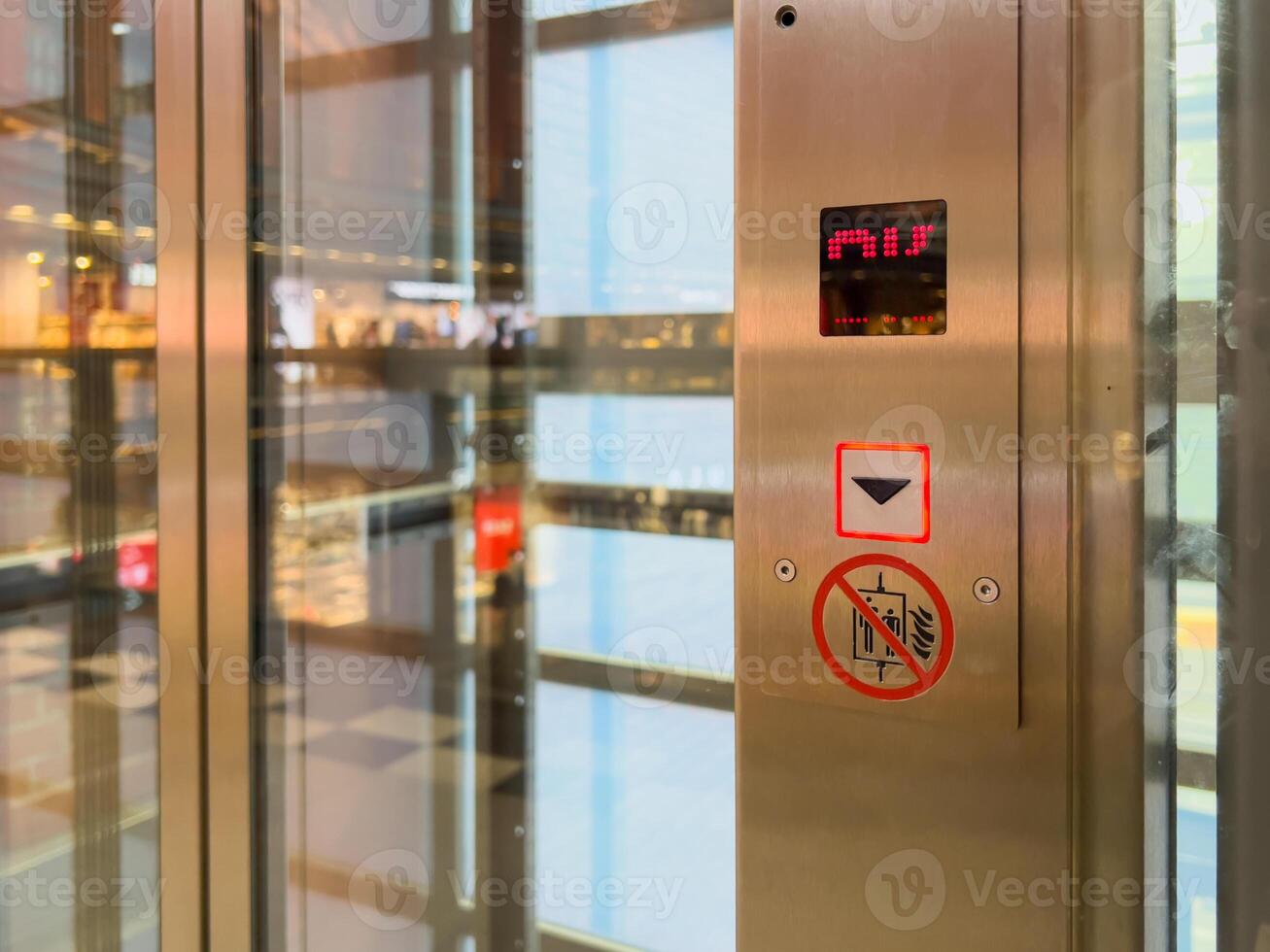 Glass elevator control panel featuring an illuminated down arrow button and floor indicator, symbolizing urban transport and modern accessibility photo