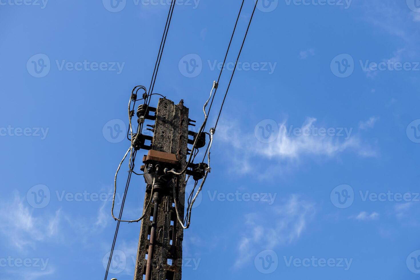 Weathered concrete utility pole supporting a complex network of electrical wires and insulators, representing vital energy infrastructure under a bright blue sky photo