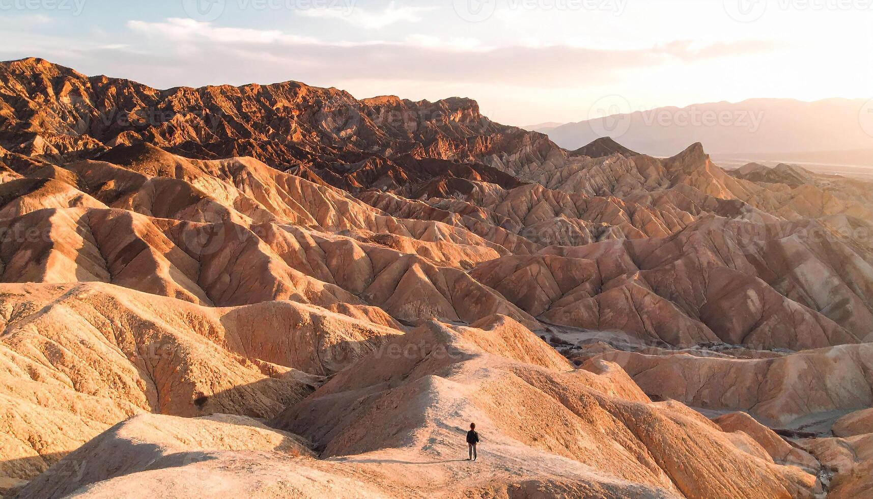 Solitary Explorer on a Ridge Overlooking Golden Death Valley Badlands photo