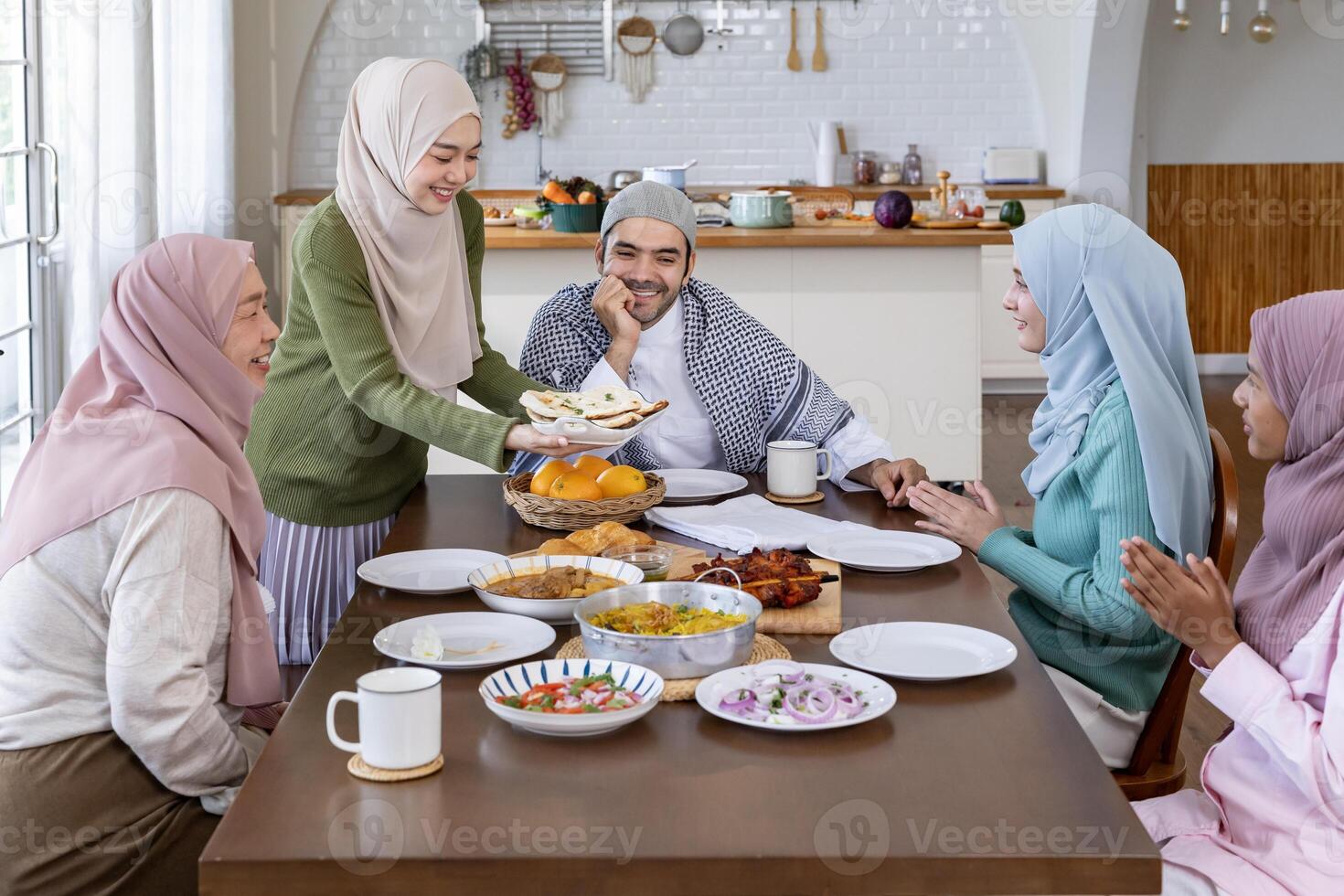 Middle eastern muslim housewife woman in hijab is serving naan bread to family dining table with her husband and relatives during Eid Mubarak, Ramadan festival for feast and gathering photo