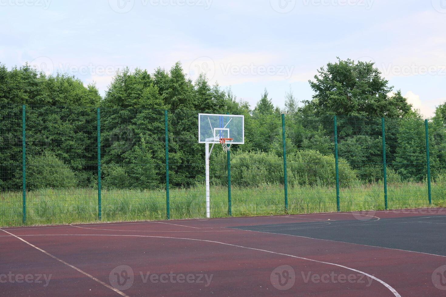 An Empty Basketball Court Nestled Within Surroundings of Lush Greenery and Trees photo