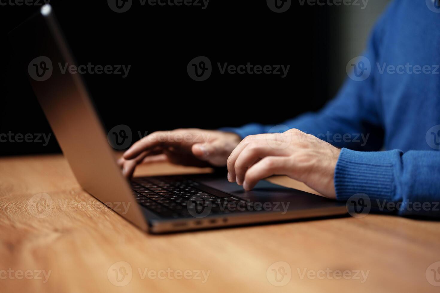Hands typing on laptop at wooden desk in a cozy setting during evening hours with soft lighting photo