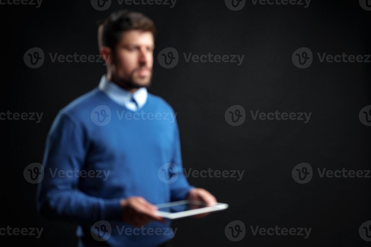 Man in blue sweater holds tablet in dark studio setting during a business presentation session photo