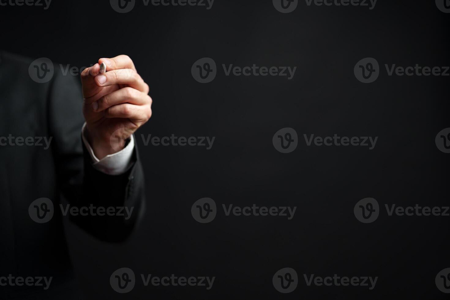 Person in formal attire holding a pen against a dark background during a business meeting or presentation photo