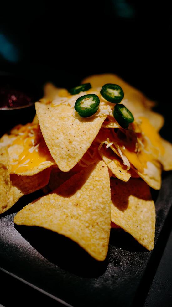 Delicious Nachos with Melted Cheese and Jalapenos on Dark Background. photo