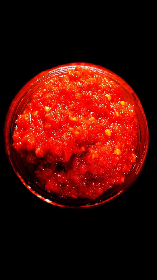 Fiery Red Pepper Paste in a Glass Jar, Isolated on Black Background. photo