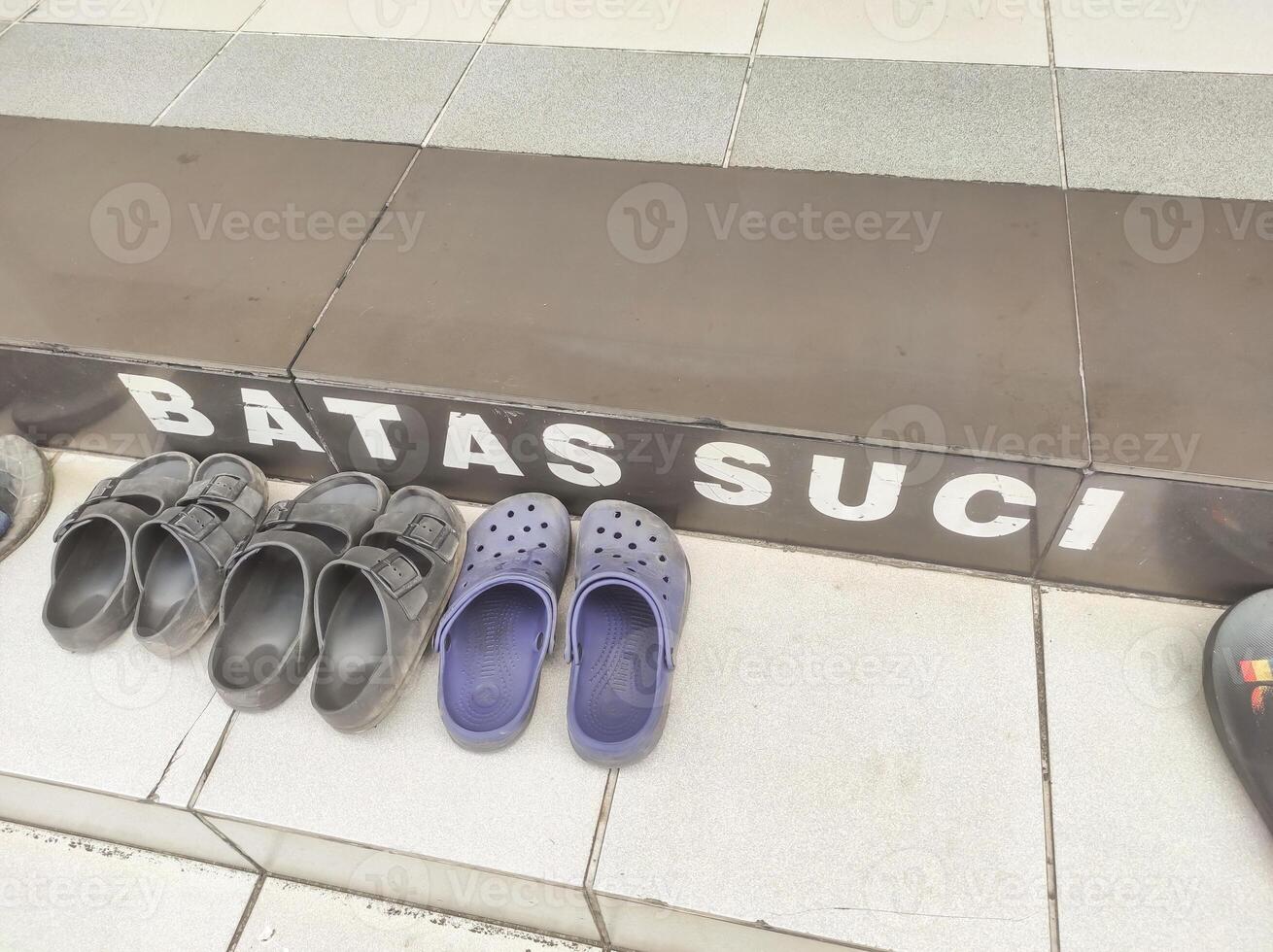 Several pairs of sandals on the floor with the inscription holy boundary. Everyone must remove their shoes upon entering the mosque area. Signs and symbols found in the mosque, Text space photo