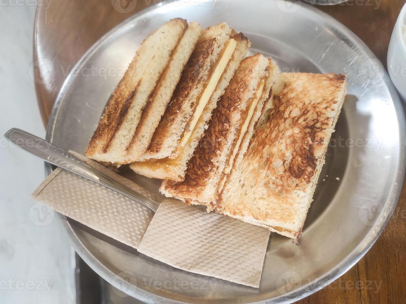 Tabletop shot of four slices of kaya toast with butter. The toast with a browned, crispy crust is served on a plate on a wooden table. Indonesian gourmet dessert. Tasty and delicious. Copy space photo