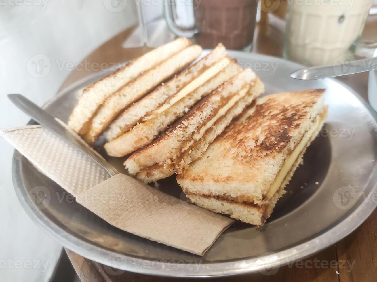 Tabletop shot of four slices of kaya toast with butter. The toast with a browned, crispy crust is served on a plate on a wooden table. Indonesian gourmet dessert. Tasty and delicious. Text space photo