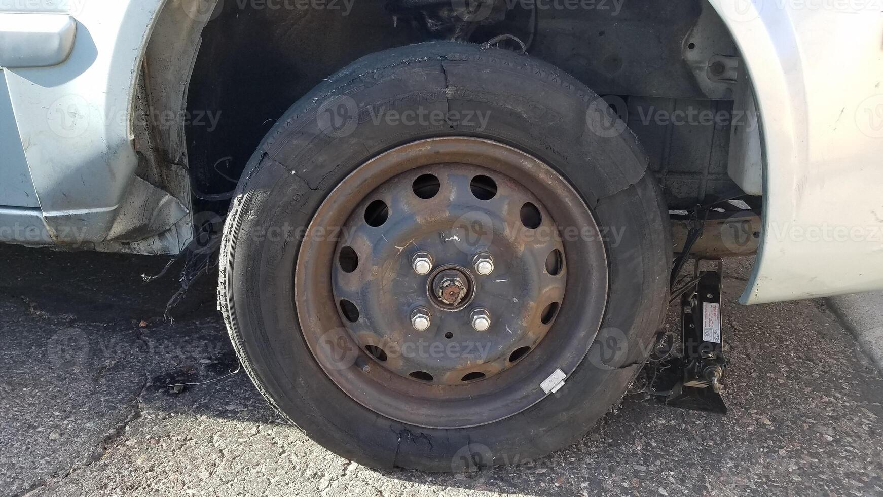 Blown Tire on a Car that Damaged the Body, Sitting on Asphalt with a Jack photo
