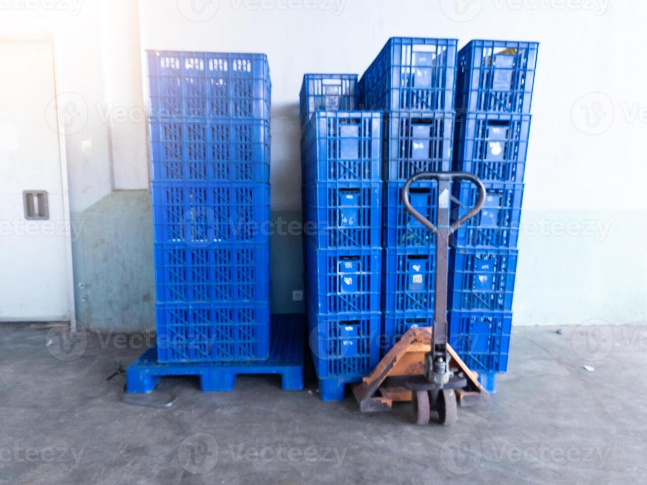 storage area with several stack of blue plastic crates ready for moving with hand pallet jack. photo