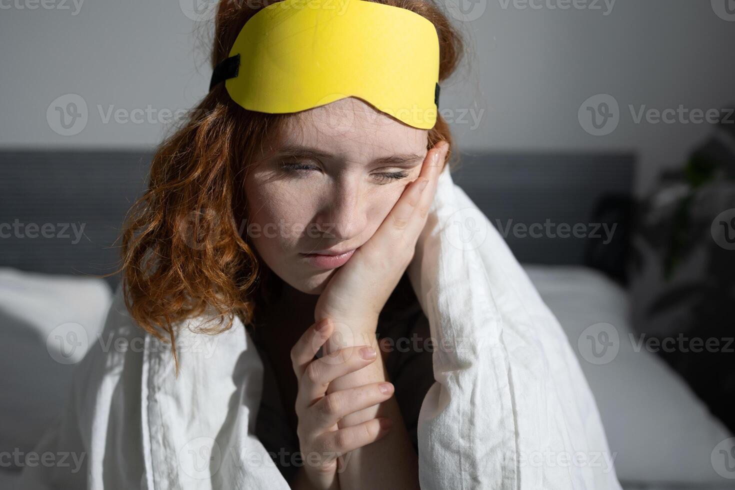 A tired woman in a sleep mask is deeply contemplating her thoughts while lying in bed photo