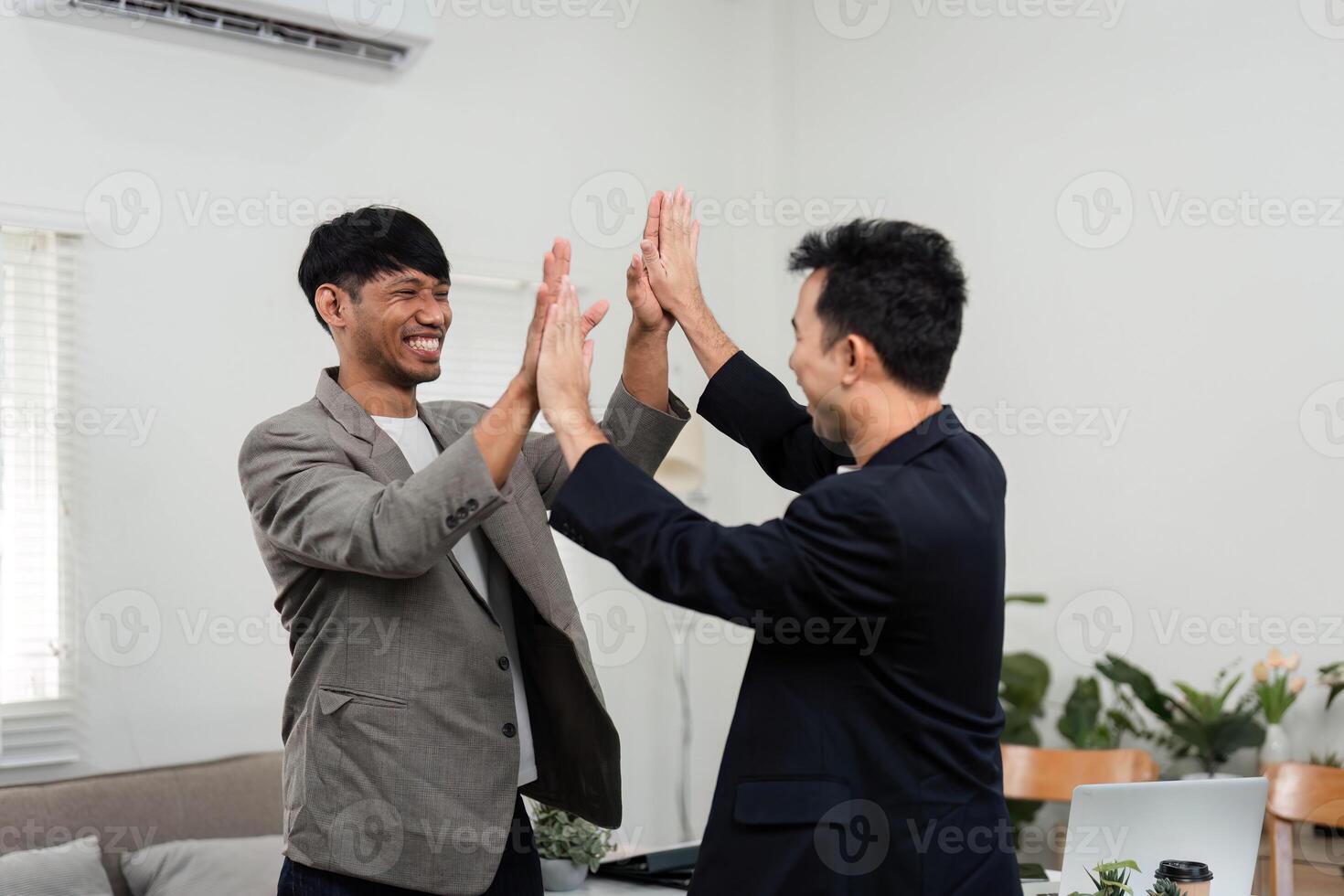 Teamwork and Business Success. Two men high-fiving in a modern office, celebrating their achievements and collaborative efforts. photo