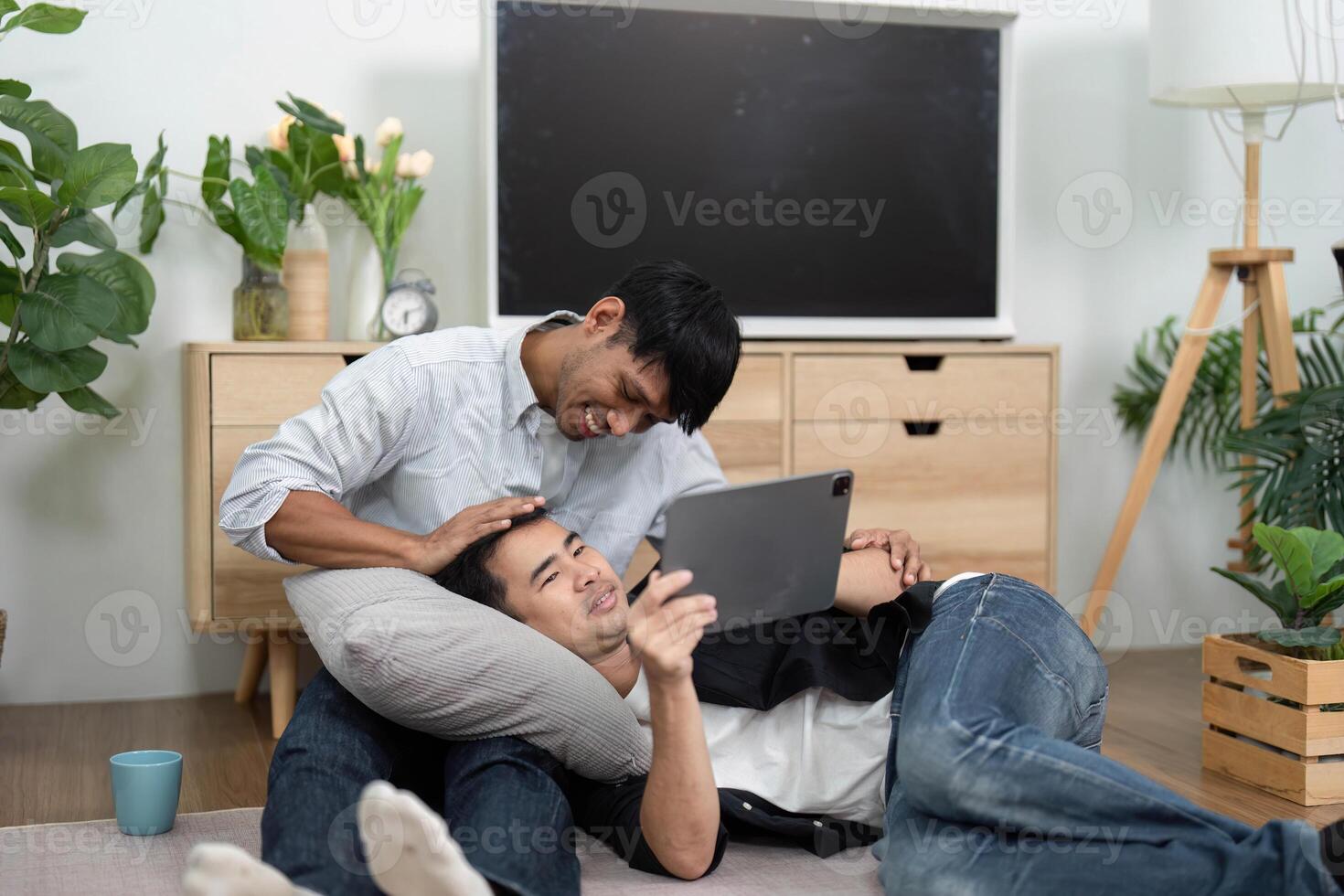 Affection and Relaxation. Two men enjoying a cozy moment while using a tablet at home. photo