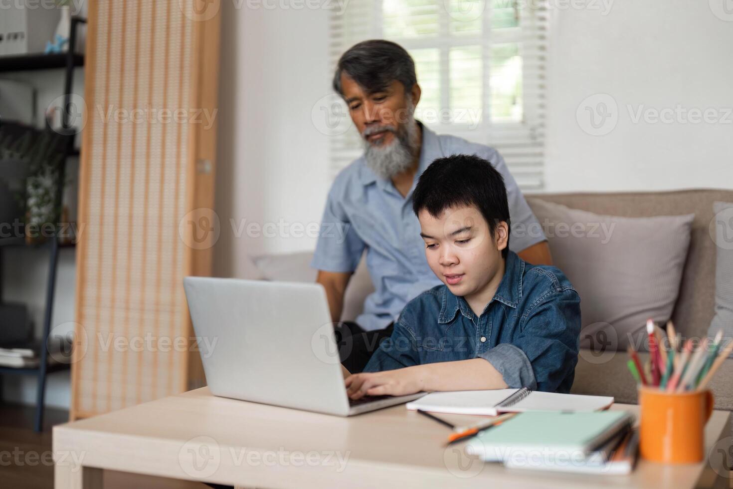 Grandfather and Grandson Learning Together. A caring grandfather assists his grandson with online activities, fostering a supportive learning environment. photo
