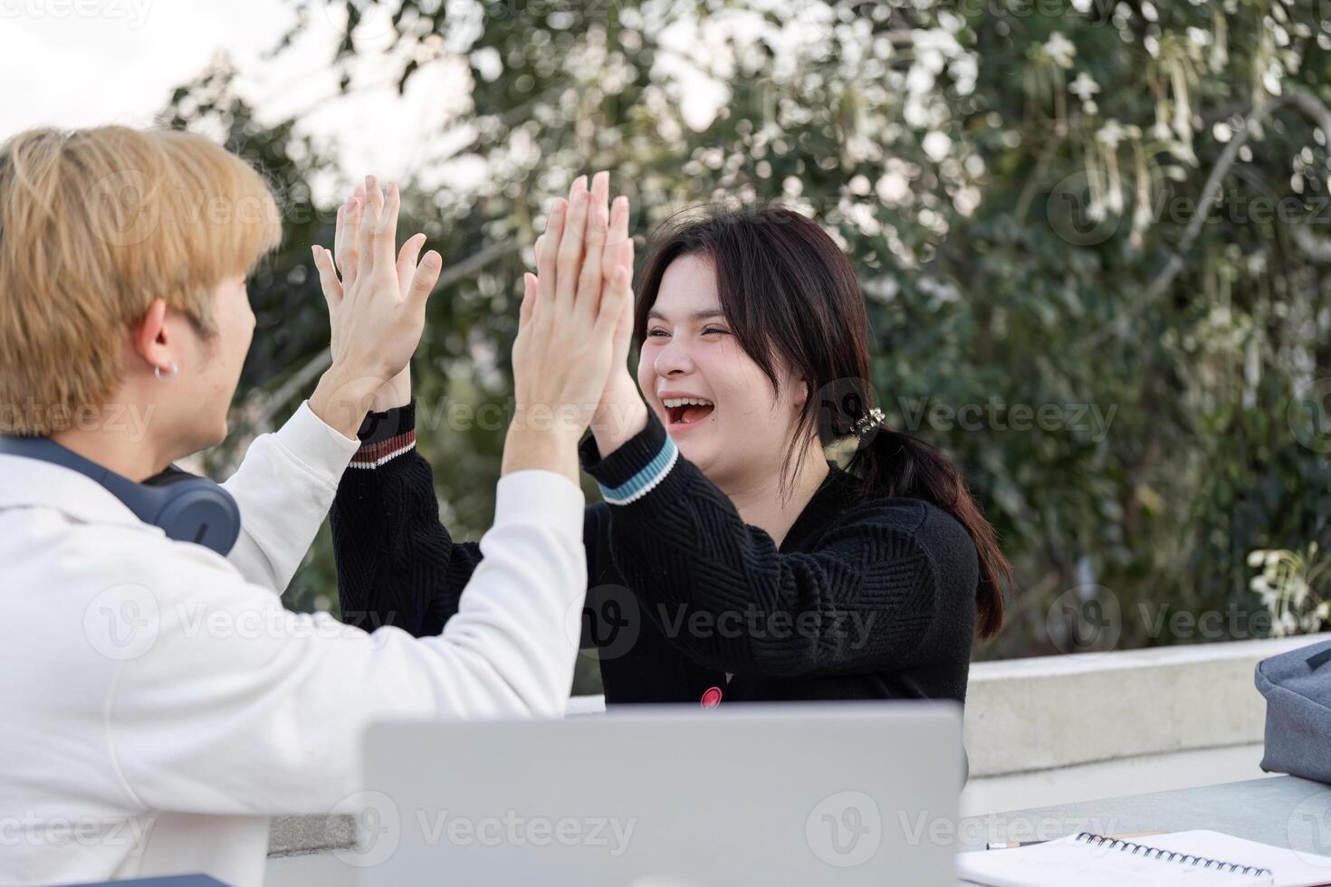 Asian College Students Celebrating Academic Success with Joyful Expressions and High Fives in Outdoor Campus Setting photo