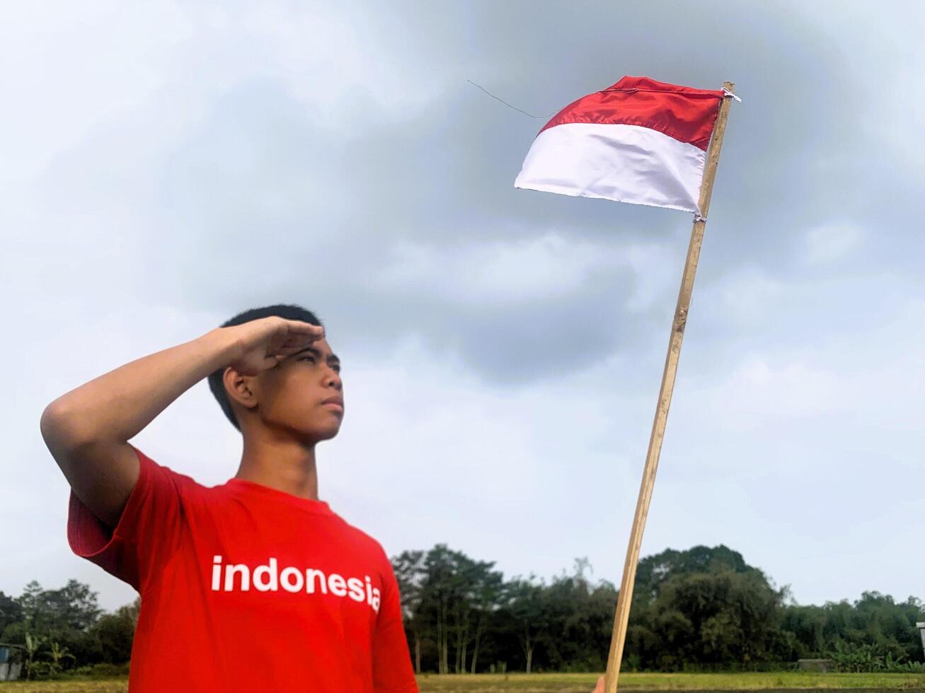 Indonesian boy with salute pose to Indonesian flag photo