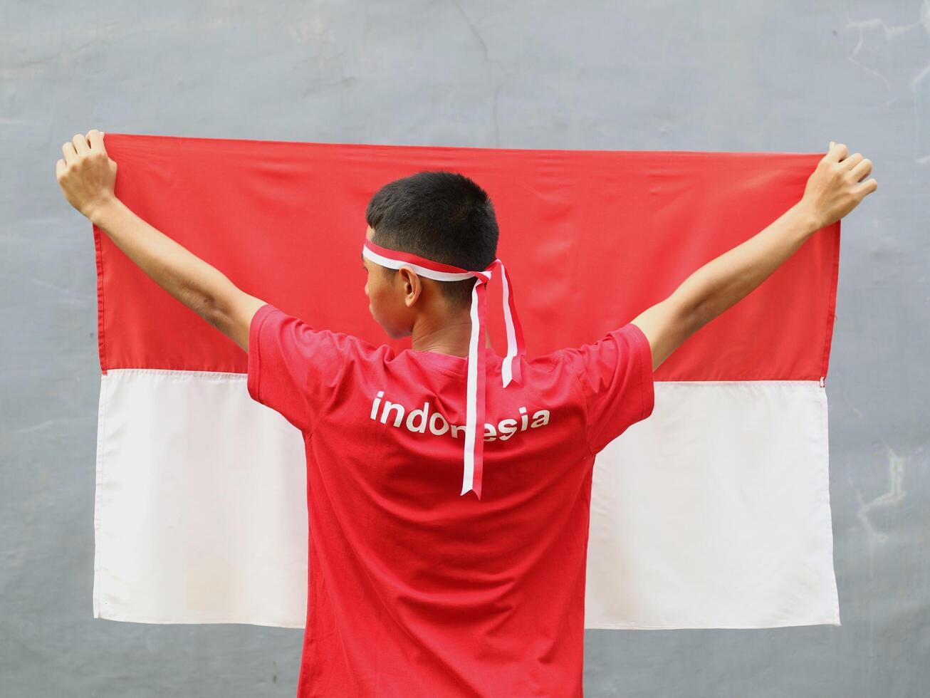 Indonesia young man wearing red white headband holding Indonesia falg against grey backgroun photo