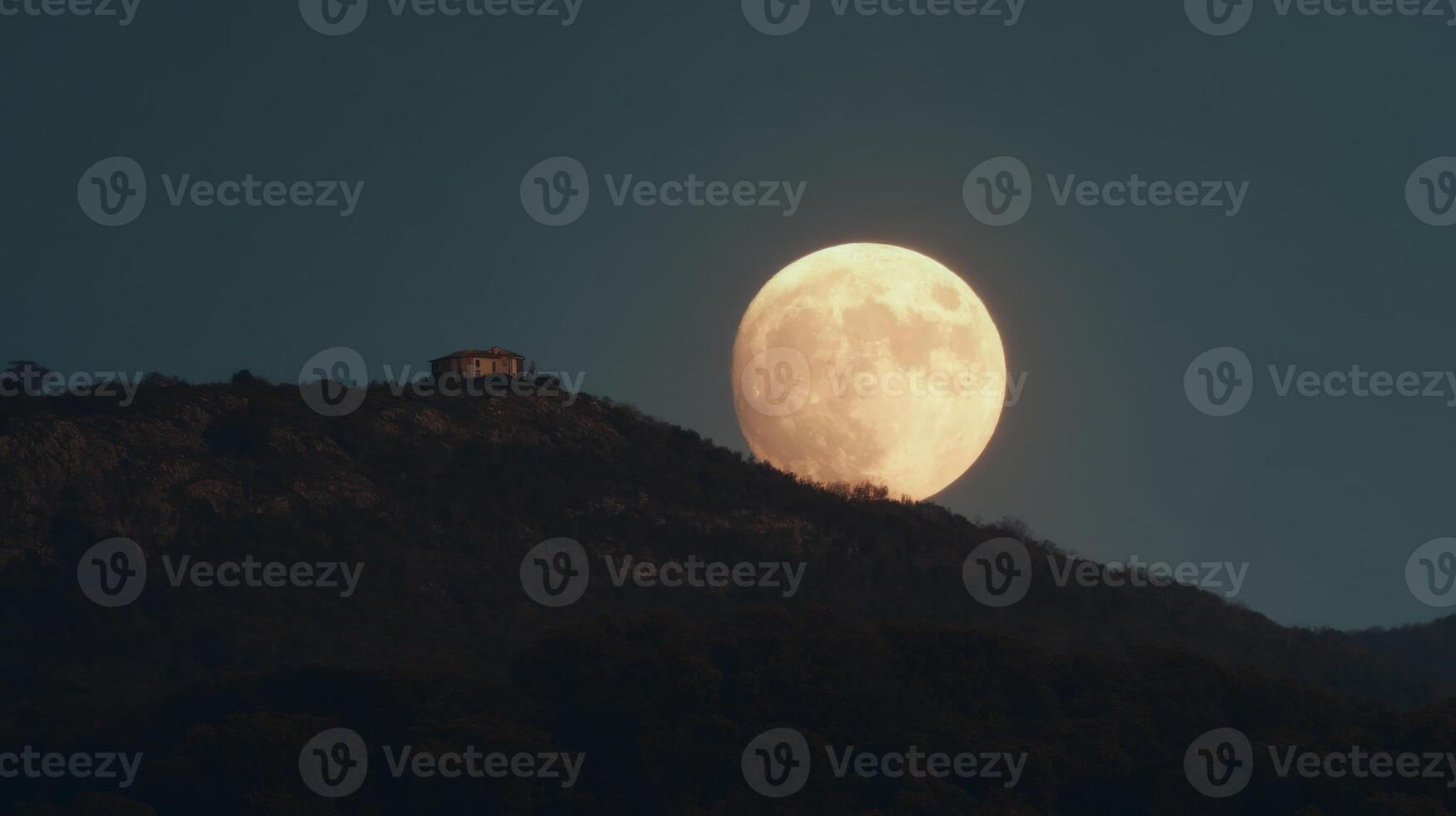 Majestic Full Moon Rising Over Serene Mountain Landscape at Dusk with Silhouette of Structure on Hilltop photo