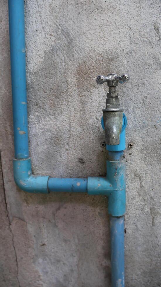 Blue PVC Water Pipes and an Old Faucet on a Concrete Wall photo
