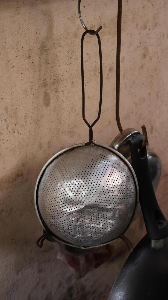 A stainless steel colander hangs in an old kitchen where the walls are splattered with grease stains photo