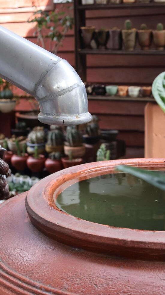 Rain Gutter Downspout Leading to a Traditional Asian Earthenware Water Jar Full of Collected Rainwater for Household Use photo