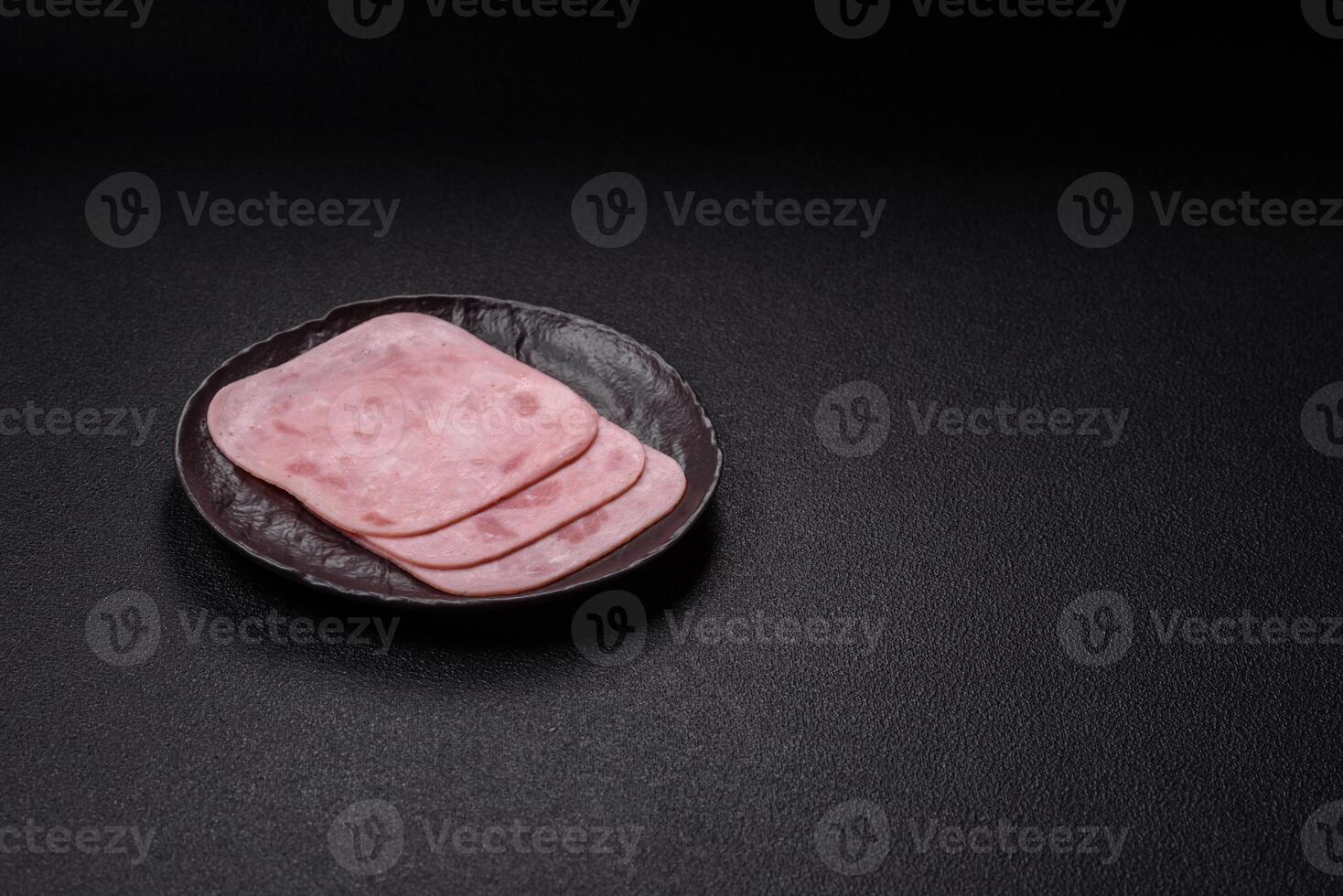 Boiled ham with salt and spices cut into slices on a black round plate photo
