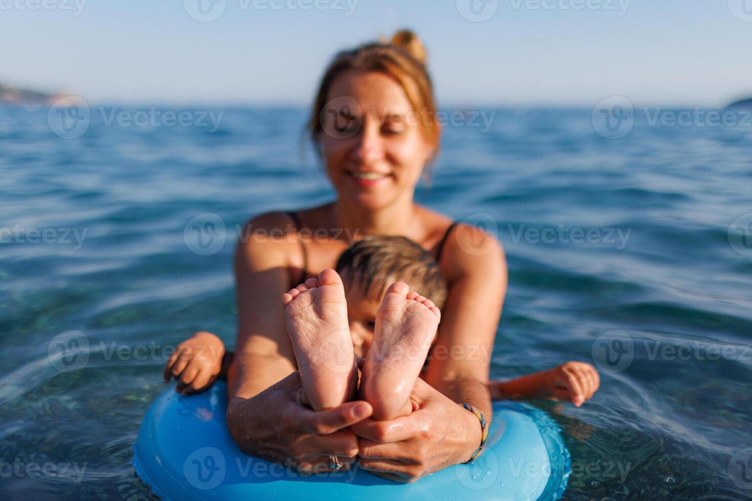 A young mother shows the legs and arms of her baby, who is sitting in an inflatable ring in the seaYoung mother shows babys legs and arms photo