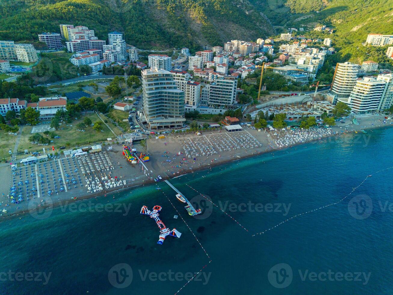 Beach with sun umbrellas, sunbeds and people relaxing in the town of Becici near Adriatic Sea against the backdrop of sunny sky photo