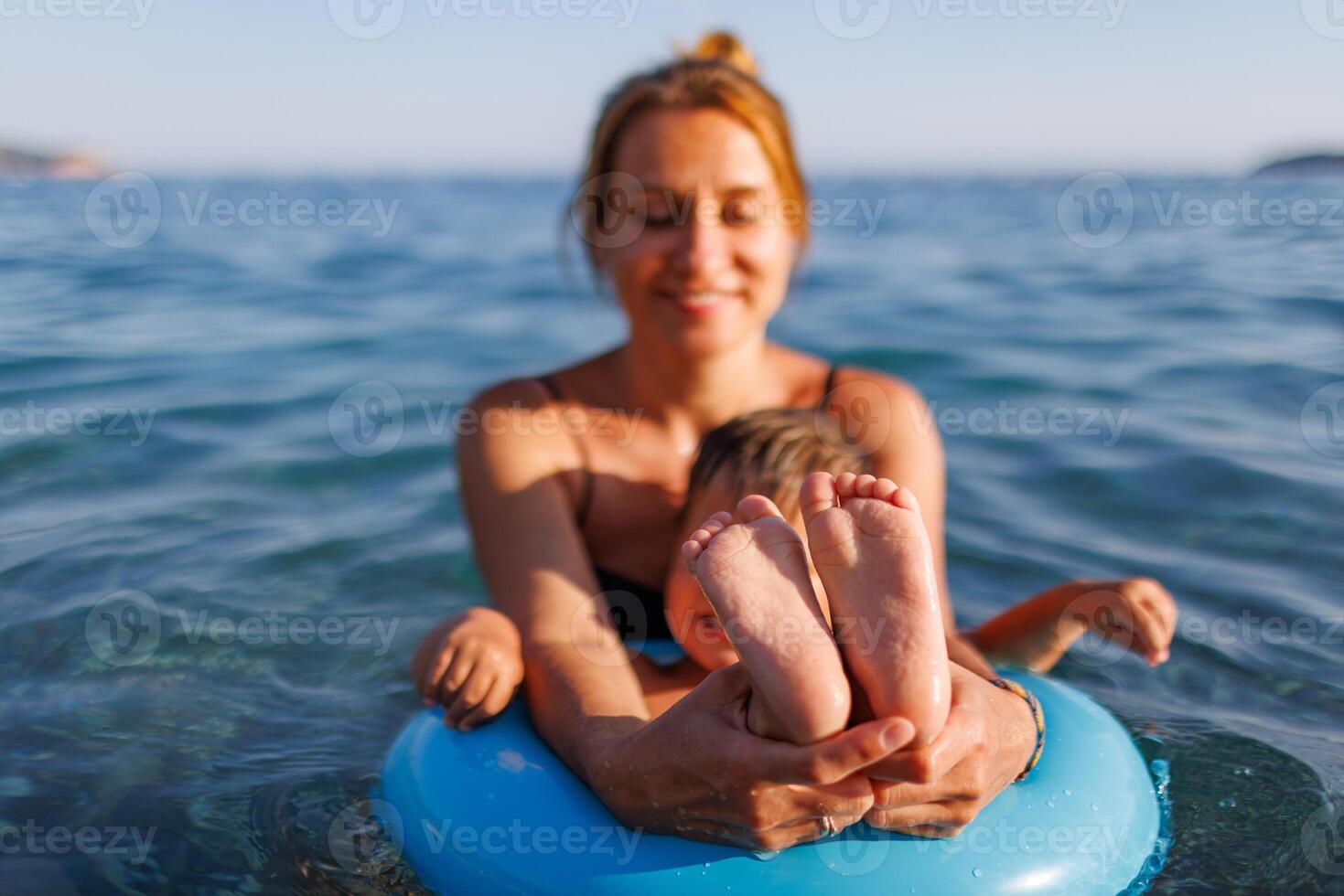 A young mother shows the legs and arms of her baby, who is sitting in an inflatable ring in the seaBaby in Inflatable Ring with Mother photo