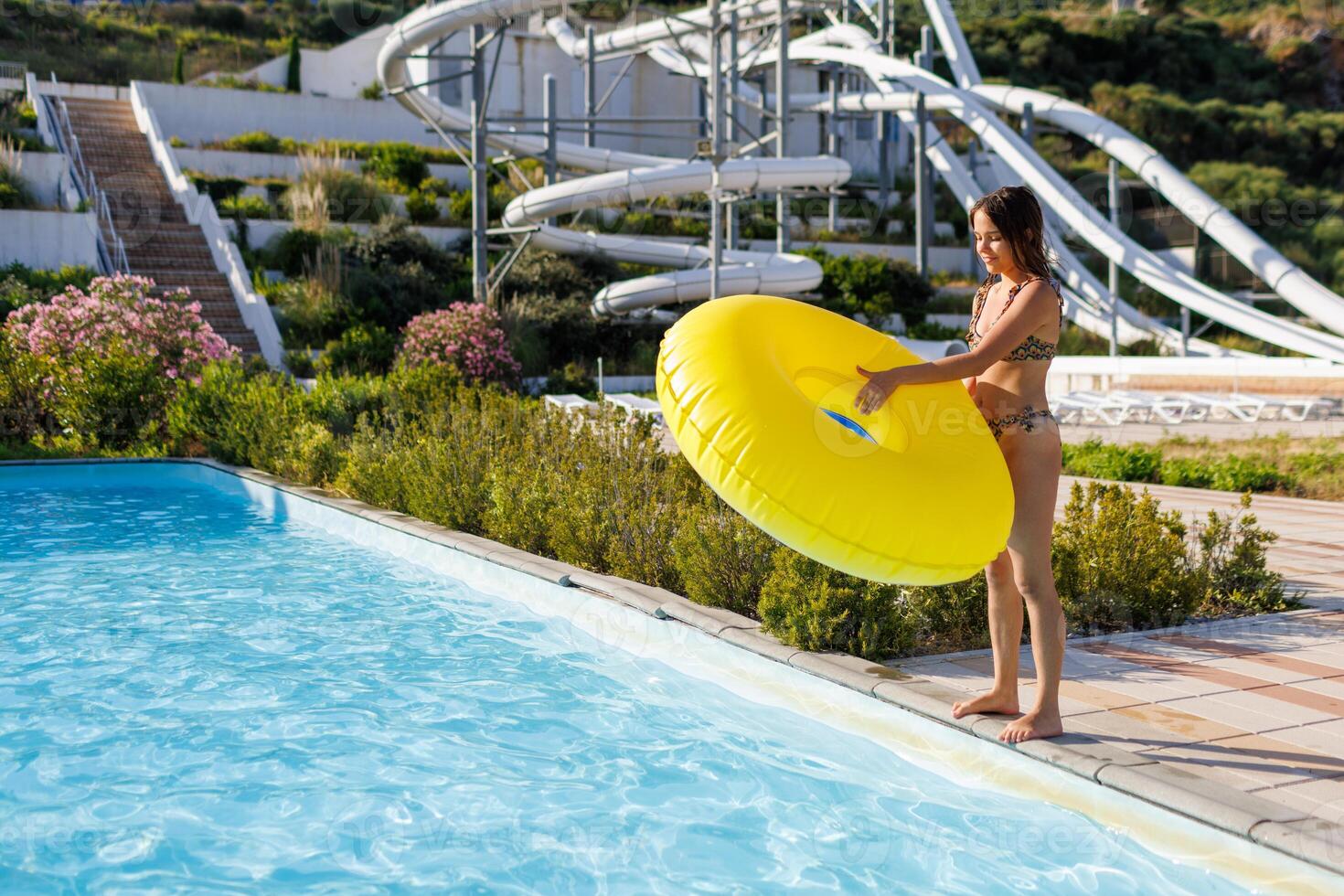 A teenage girl stands at the edge of the pool and holds a large photo