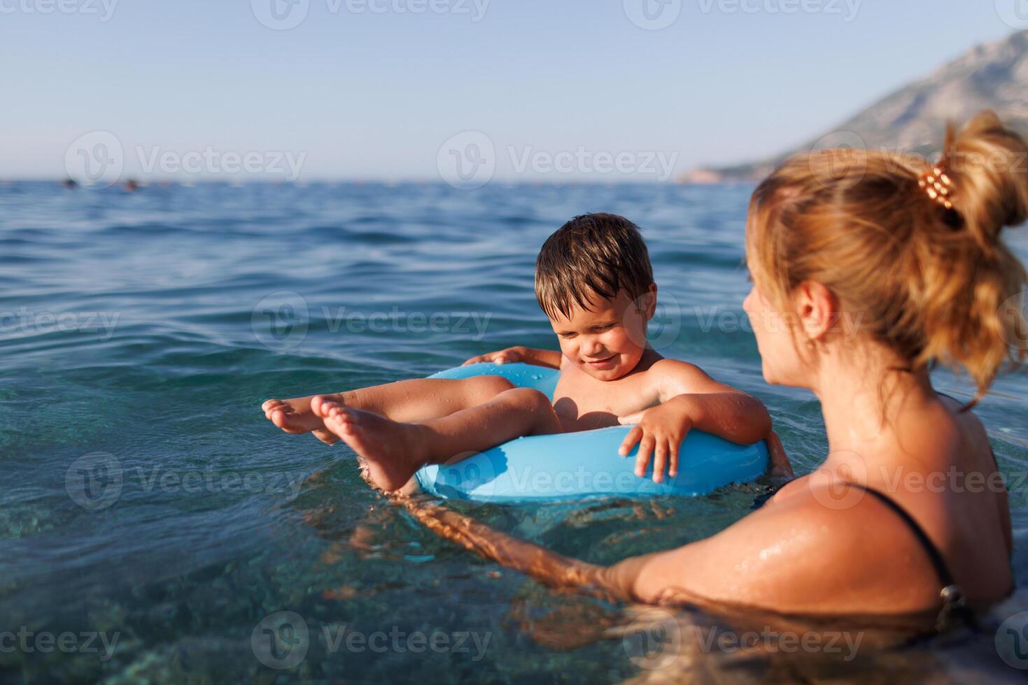 Caring mother rides her son on an inflatable ring in the seaCaring mother rides son on inflatable ring seaCaring mother rides son on inflatable ring sea photo