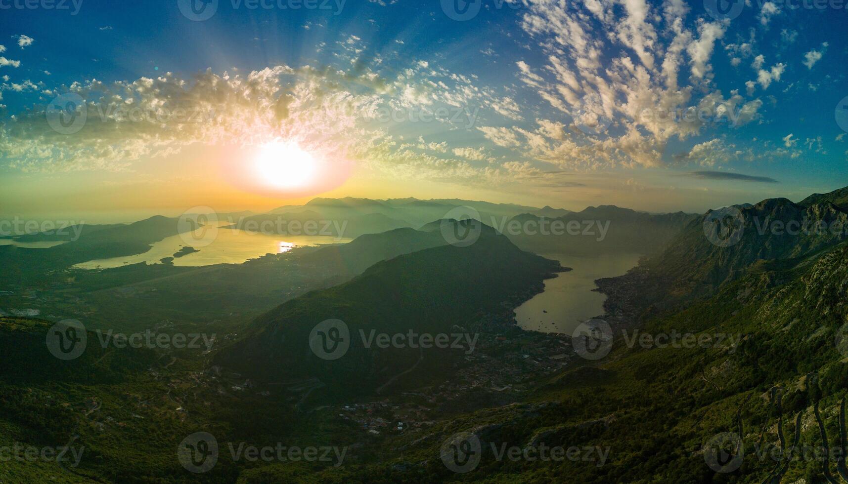 Panorama of dazzling sun in the evening sky illuminates all the peaks of the Balkan Montenegrin mountains and the coast of Kotor Bay photo