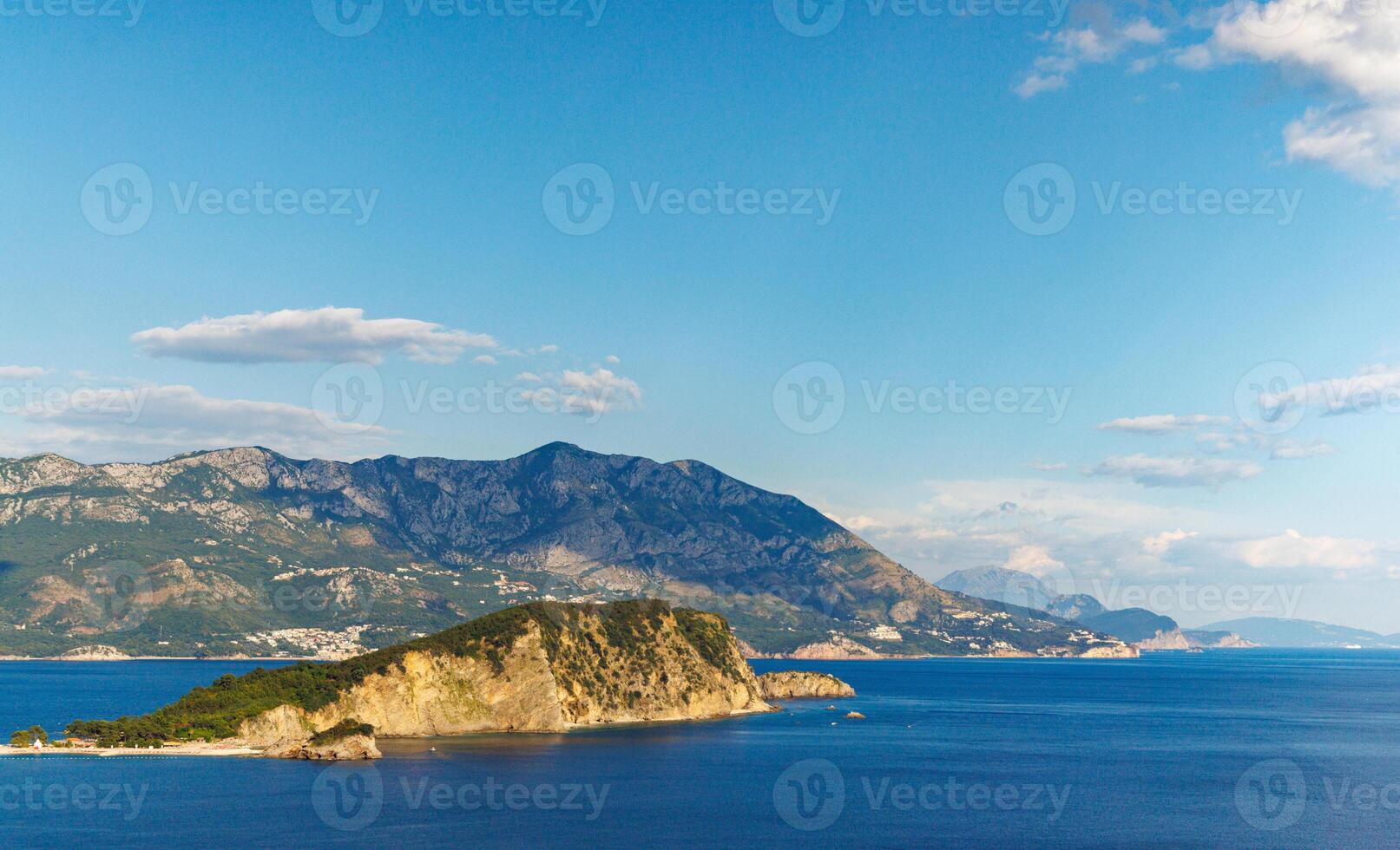 Island of St. Nicholas with vegetation on shores in the Adriatic Sea against the backdrop of coastal towns, the Montenegrin mountains and clear skyIsland of St Nicholas with Coastal Towns photo