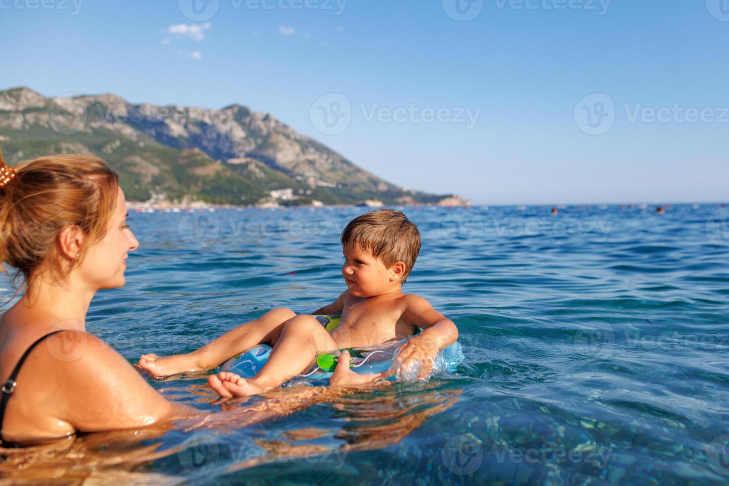 Caring mother rides her son on an inflatable ring in the seaMother carries son on inflatable ring in sea photo