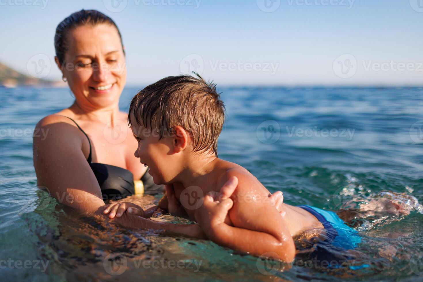 Cheerful mother plays with her son in the seaMother plays happily with son in seaCheerful mother plays with son in sea photo